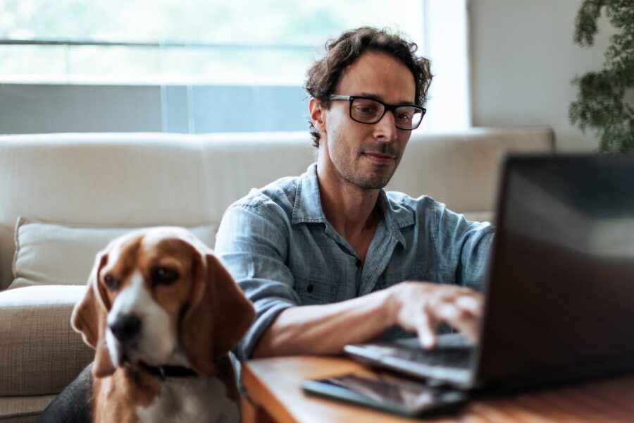 A man comfortably working at home on his laptop, sitting on the floor with his Beagle dog by his side.
