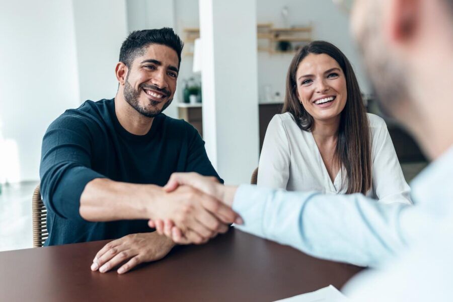 Happy young couple shaking hands with a male agent