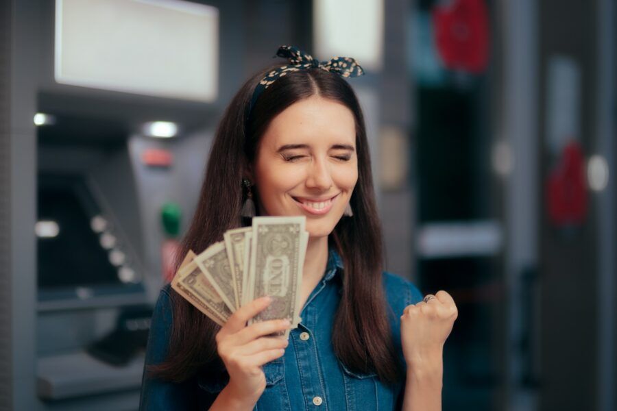 Happy woman holding fanned-out cash in front of an ATM.