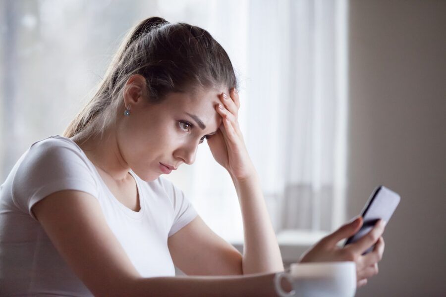 Sad young woman looking at smartphone frustrated by credit card denial.