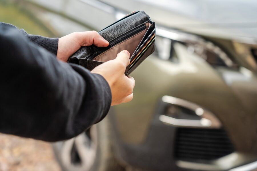 A person holding an empty wallet in their hands stands in front of a car.