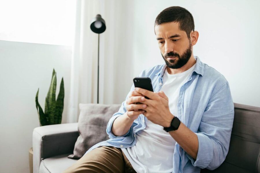 Focused man using his smartphone while sitting on a sofa in a living room