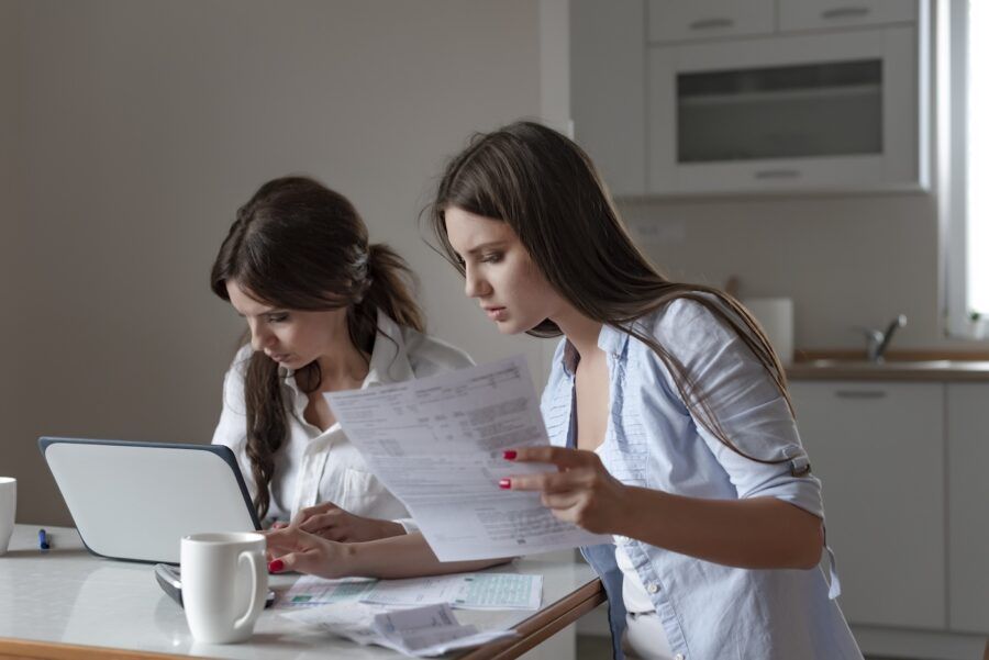 Two women working on finances at a kitchen table, looking stressed.