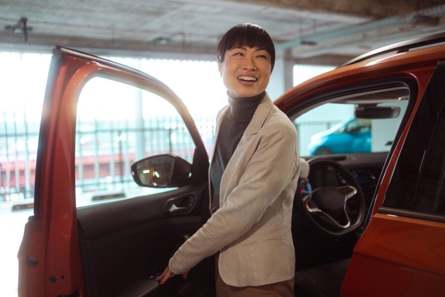 Photo of a cheerful woman entering a car and closing the car door.