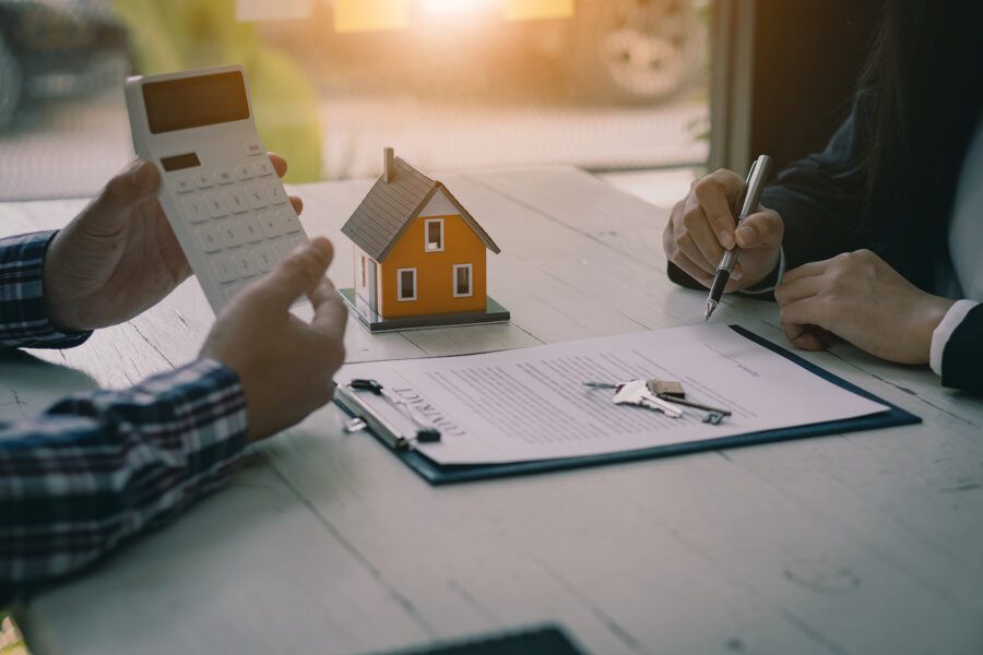 Person considering tapping into home equity holding a callculator, a table with a small model house and keys on top of a contract.