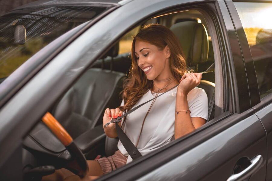 Smiling woman sits in the driver’s seat of a car fastening a seat belt
