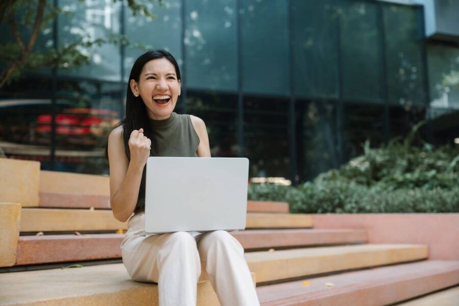 Excited woman using her laptop while sitting on outdoor steps