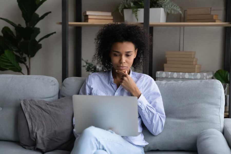 Pensive young woman using her laptop in the living room