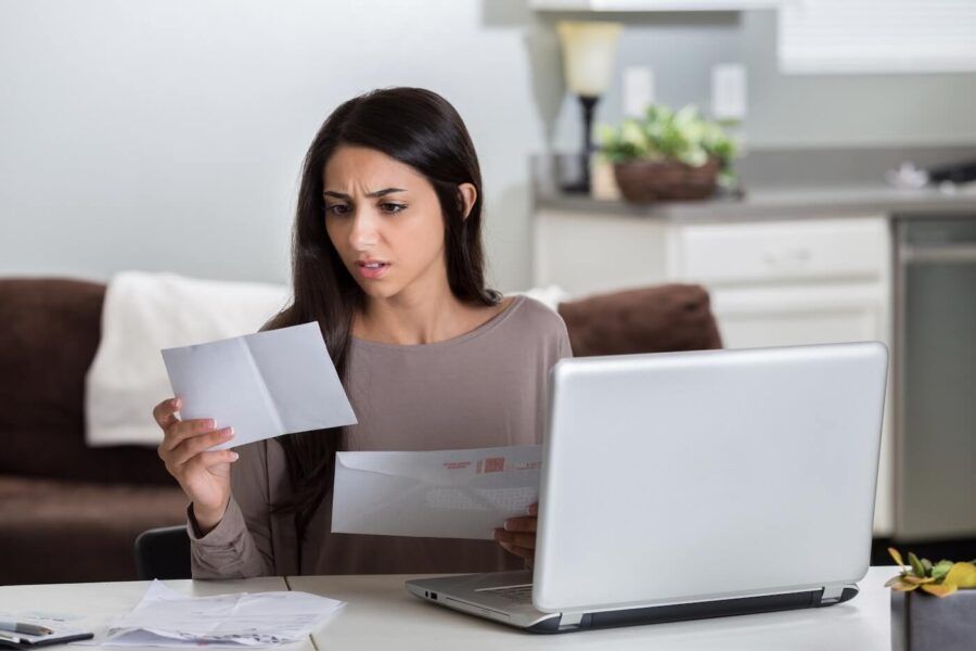 Concerned young woman reading a letter, with a laptop open beside her on the table