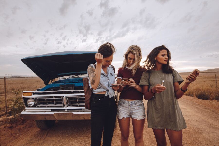 Three female friends making a phone call after their car break down on country road.