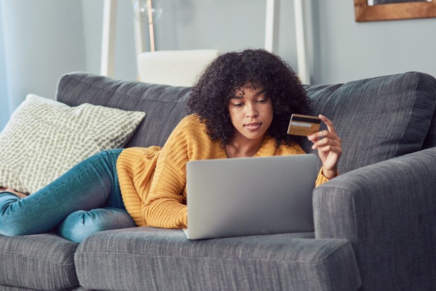 Shot of a young woman using a laptop and credit card on the sofa at home.