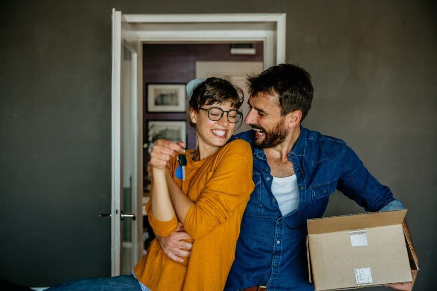 Portrait of a happy woman and a man, holding a moving box and keys from the new first house