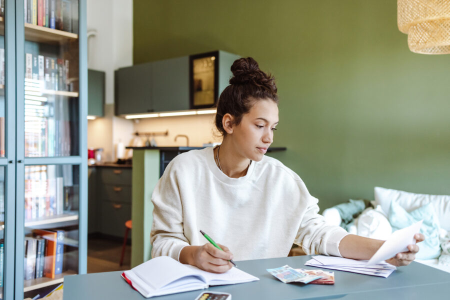A young woman in a beige sweater sitting at the table and calculating finances