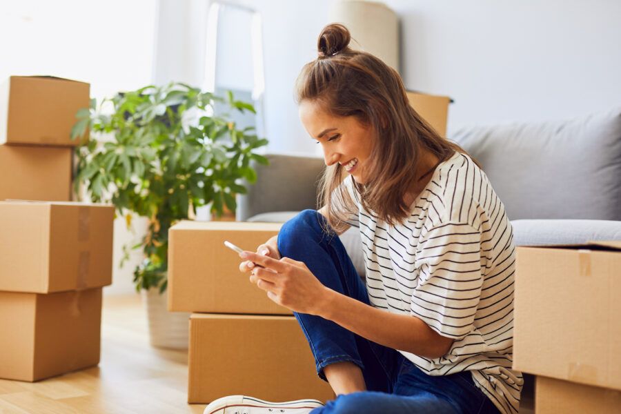 A woman sitting on the floor applying for a new credit card on her mobile phone while moving to new apartment