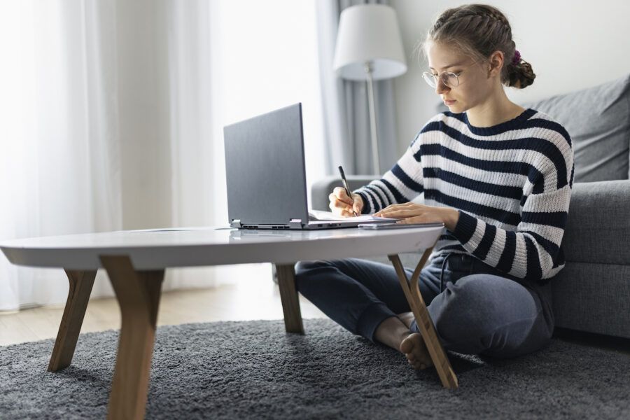 A woman assessing her debt using the 20/10 rule, working on her laptop on the coffee table.