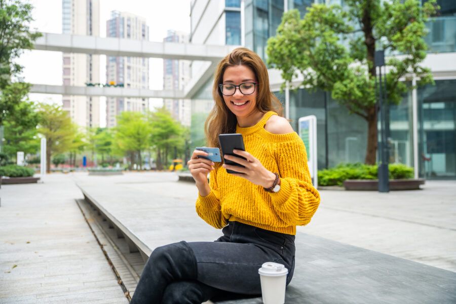 Woman sitting outside holding credit card and phone