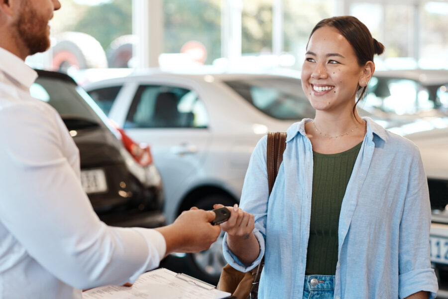 A woman in a car dealership being handed the keys to her ner car by a car salesman