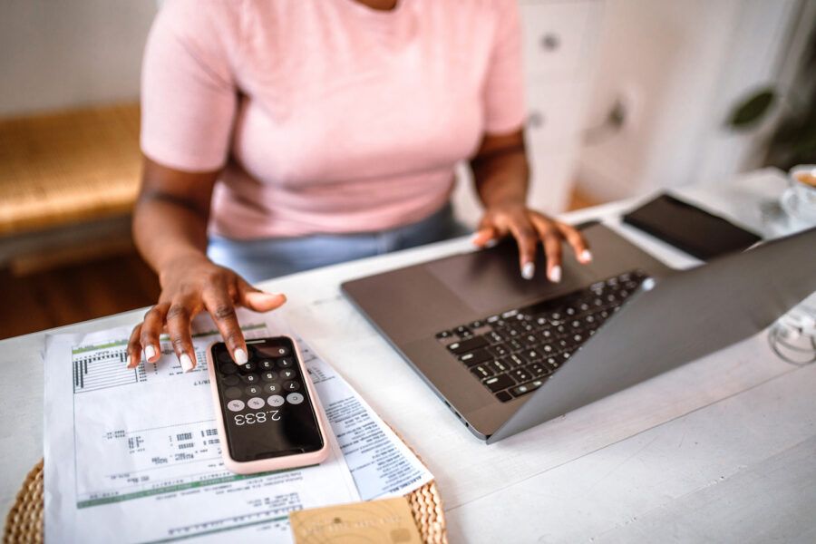 Woman managing home finances using smart phone calculator app and laptop to calculate loan amounts.