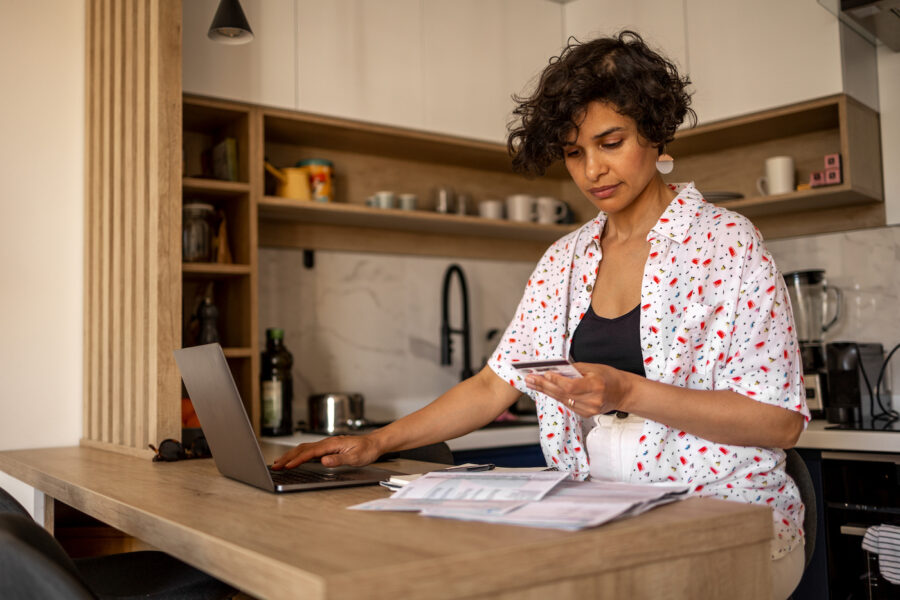 Woman checking her CD at home, doing finances on her laptop at the kitchen counter.