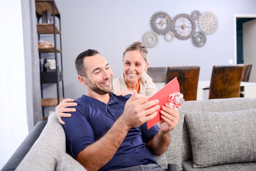 A young woman offering gift money in envelope gift to a man sitting on the couch