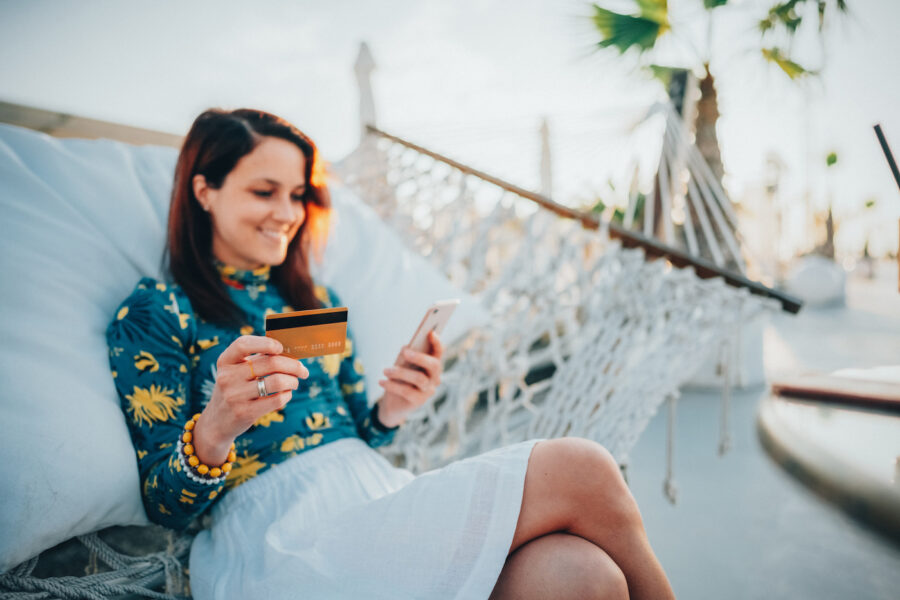 Relaxed woman in hammock using rewards credit card for online shopping on mobile phone