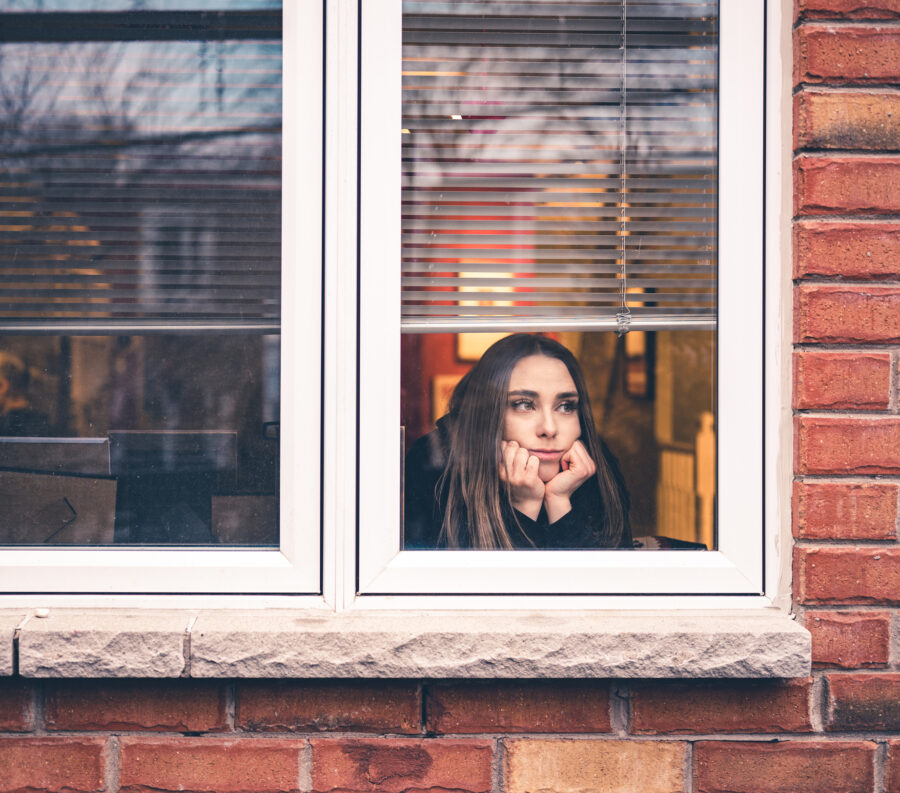 Woman longingly gazes out the window of her home