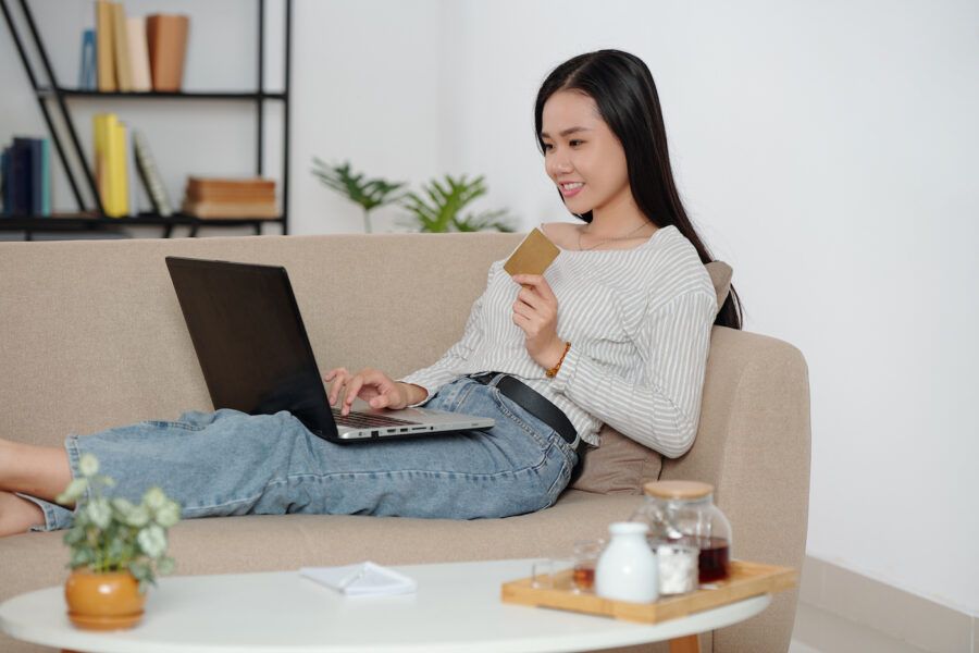 Woman looking up online accounts laying on couch holding a card.