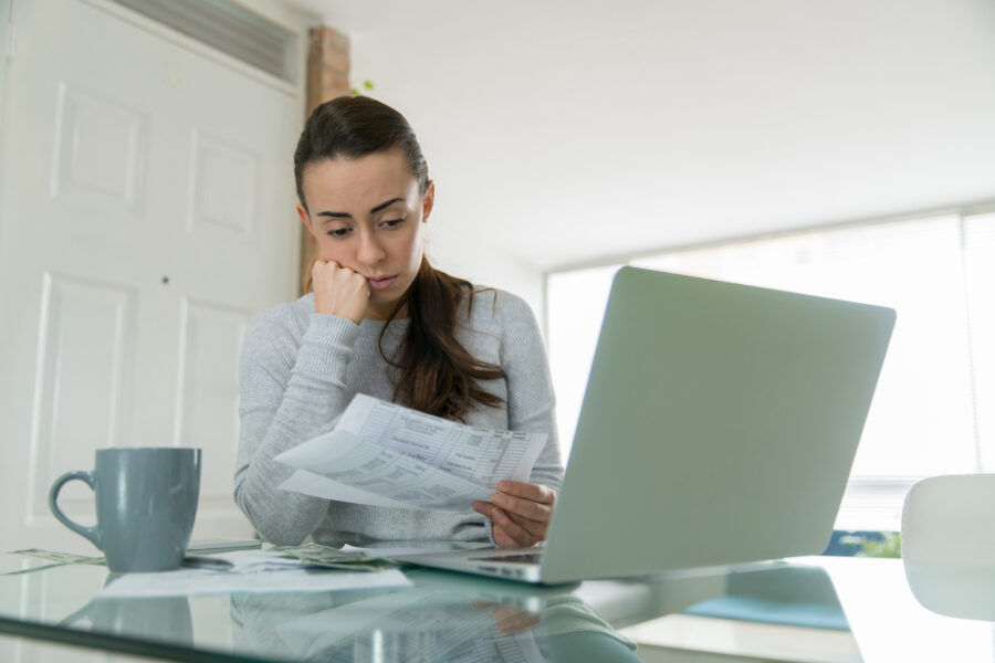 Woman looking worried while considering using her emergency savings fund, looking at paper bills and laptop