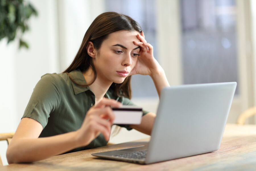 Woman looking at computer holding credit card, taking steps to prevent fraud