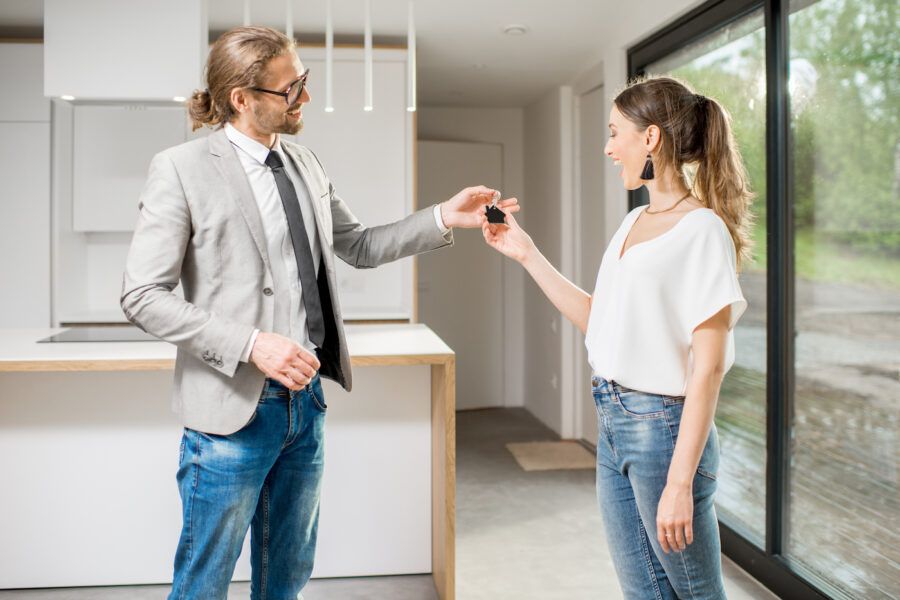 Happy young woman buyer standing and shaking hands with realtor, receiving keys of a new house.