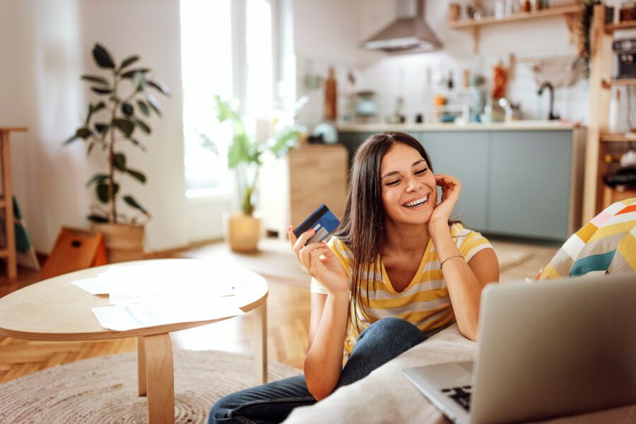 A woman holding her credit card and looking at her laptop, happy about having zero liability fraud protection from her credit card isssuer.