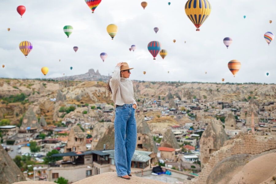 woman standing on overlook surrouunded by hot air balloons in the sky.