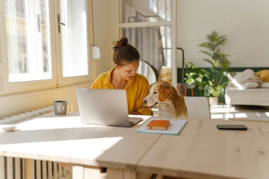 Smiling young woman working from home, with her laptop open and her dog sitting beside her