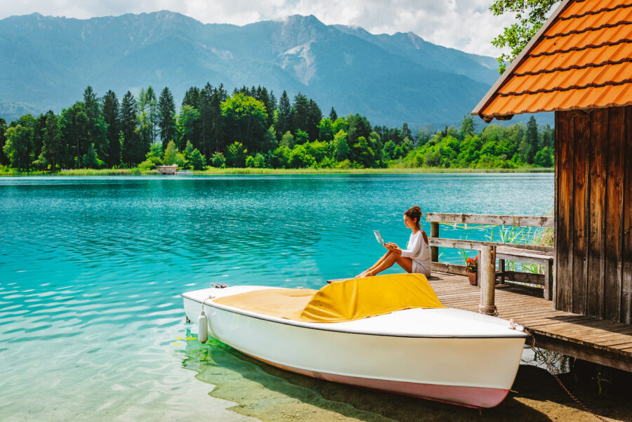 A woman working remotely from her laptop, sitting on a lakeside dock at beautiful Lake Faak in Austria, Europe