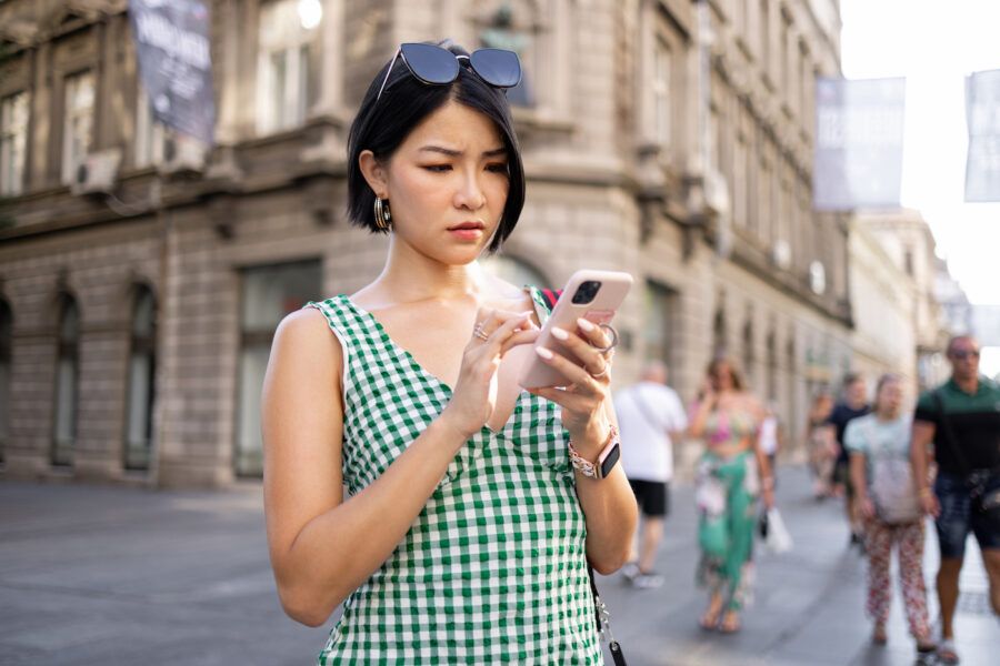 Worried woman realizing she sent a payment to the wrong person, holding her phone on a street corner.