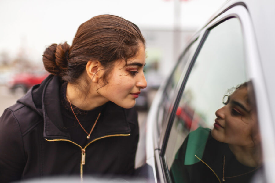 Young woman looking into a car window contemplating buying a car
