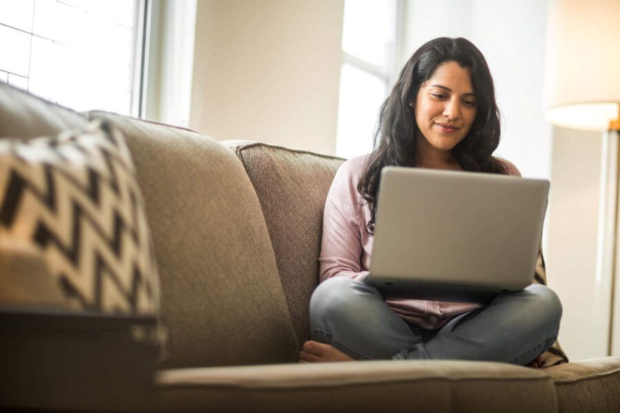 Young woman seated cross-legged on a sofa researching buy now pay later on laptop.