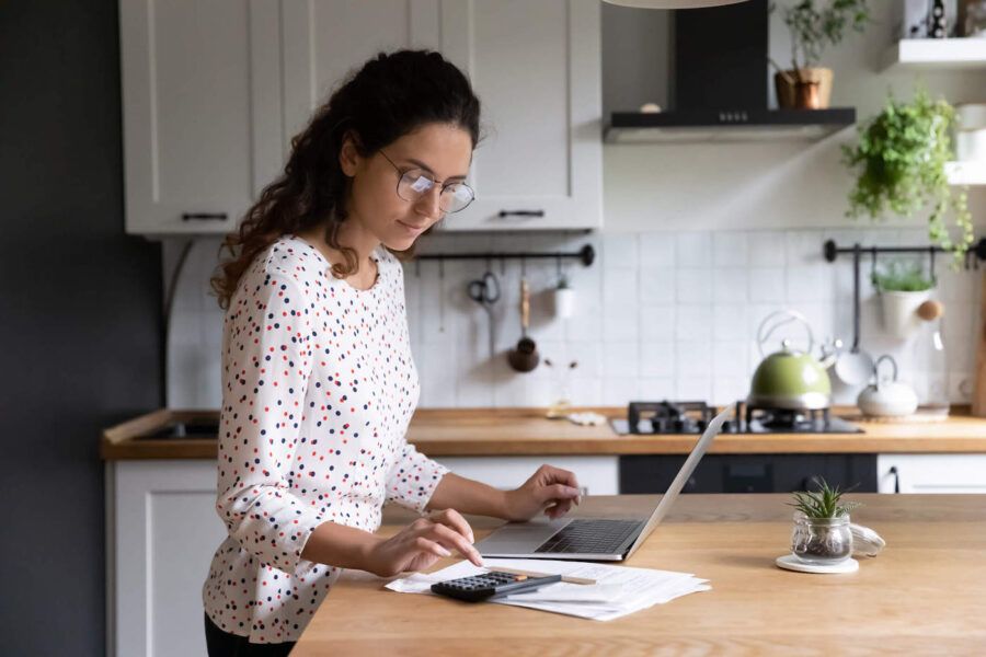 Young woman using calculator on kitchen island.