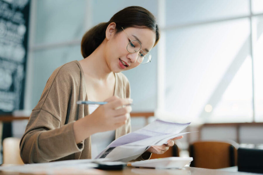 Young woman with eyeglasses smiling as she looks down at the papers she's holding.